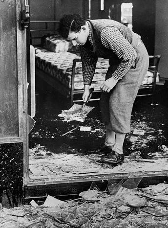 Un barbat curata geamul spart dupa Kristallnacht